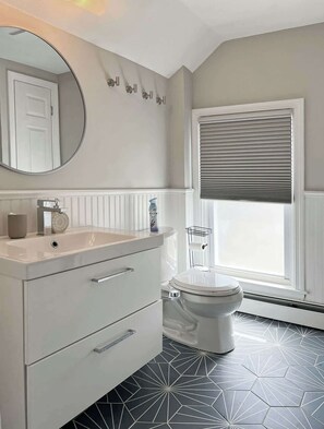 A bathroom with a white vanity, a round mirror, a toilet, and a window with blinds. - Downtown Warren Top Floor Loft 3BR: Spa | Walkable (Warren)