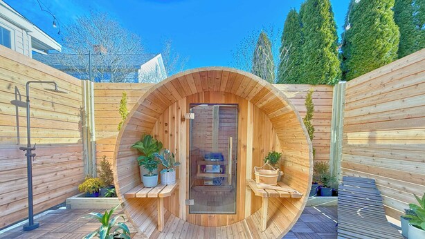 Una sauna de madera con diseño circular, rodeada de plantas en macetas y bancos de madera.