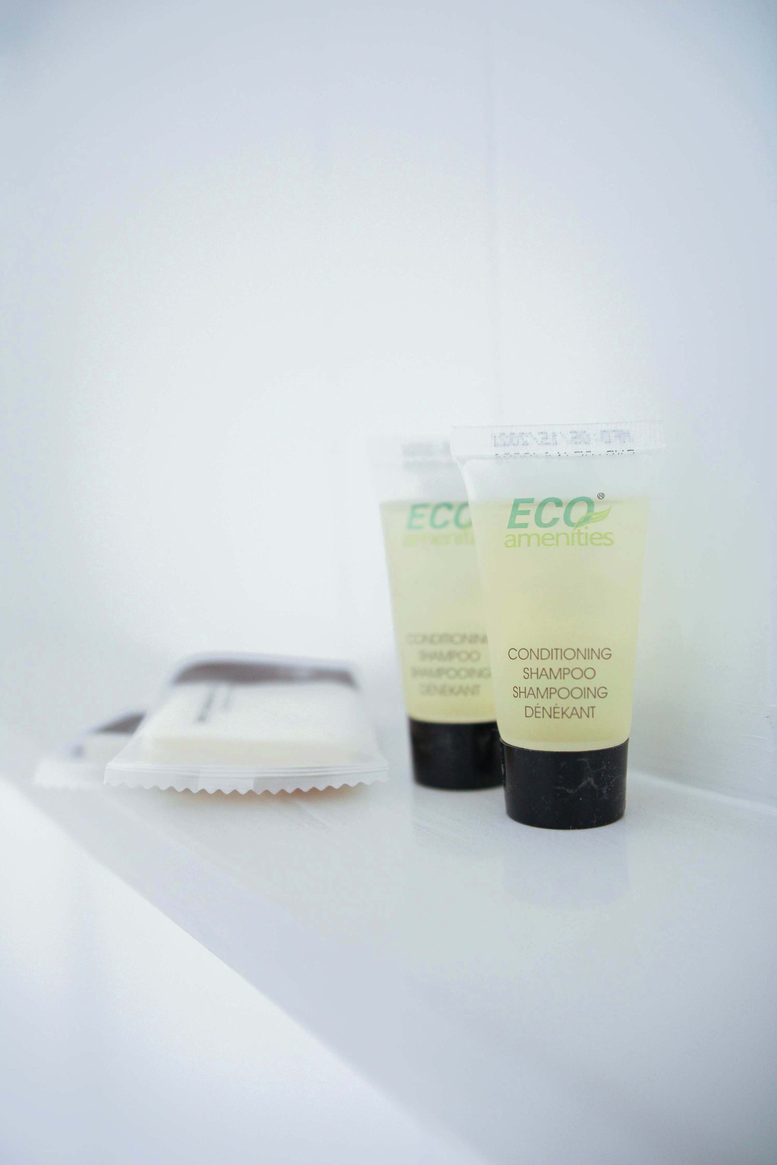 Two tubes of ECO amenities conditioning shampoo and a razor on a white surface.