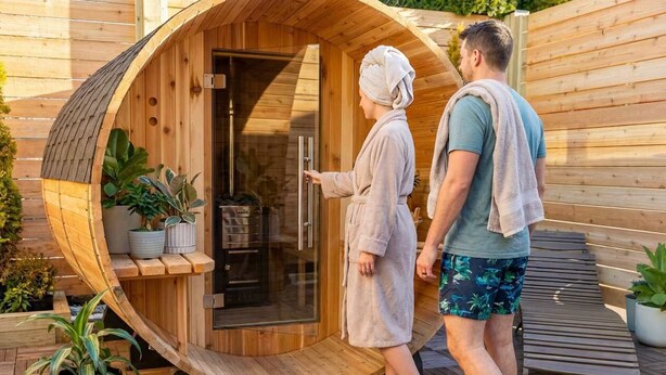 Uma sauna de madeira com exterior curvo, porta de vidro e um banco no interior.