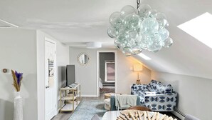 Ein modernes Schlafzimmer im Loft-Stil mit einem großen Oberlicht, einer außergewöhnlichen Glaskristallleuchtreihe und einer gemütlichen Sitzecke mit gemusterten Kissen.
