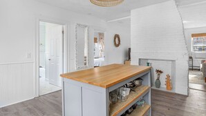 Eine Küche mit Holztischplatte, weißen Schränken, einer hängenden Lampenschirm aus Weide und einer weißen Ziegelwand.