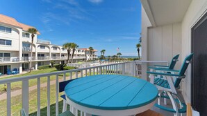 A balcony with a table and chairs, overlooking a pool area and a building with multiple balconies. - Beachfront Getaway in St. Augustine (St. Augustine)
