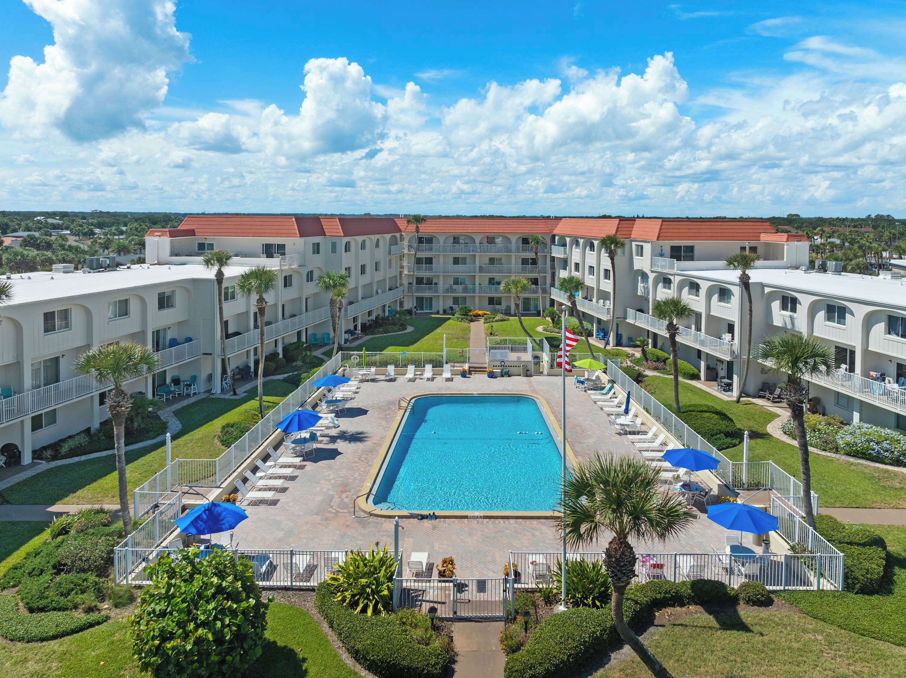 A hotel with a central swimming pool, multiple balconies, and a well-maintained lawn.