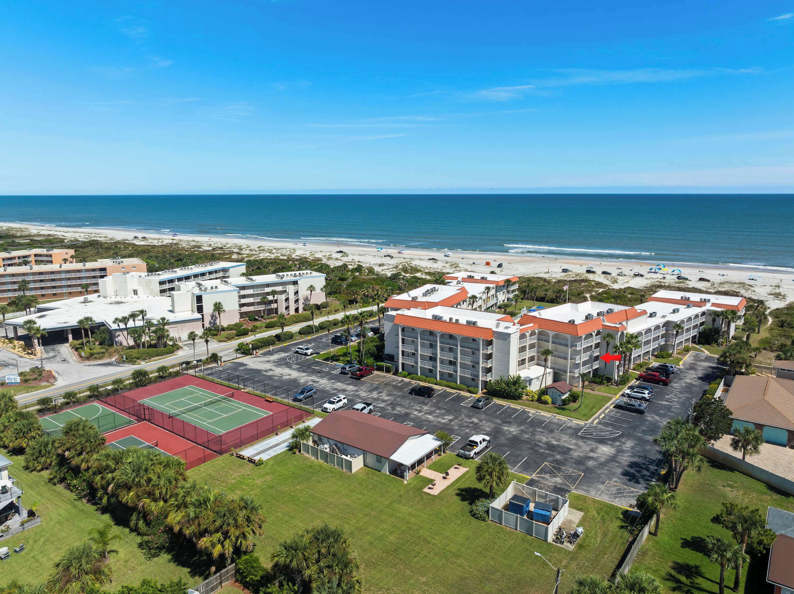 Ein Hotel mit mehreren Gebäuden, einem Parkplatz und einem Strand im Hintergrund.
