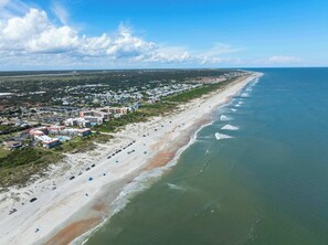 Vista aérea de una zona costera con una playa, una hilera de hoteles y un cielo despejado.