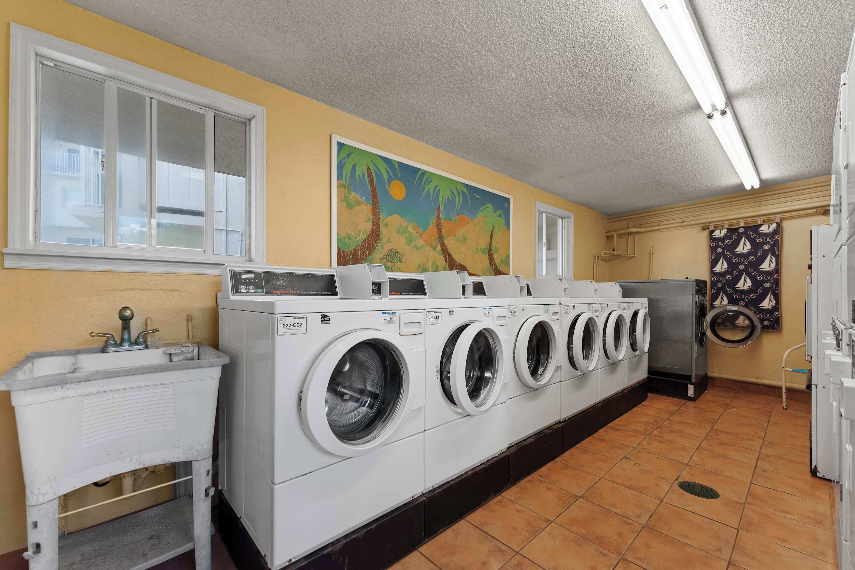 A laundry room with multiple washing machines, a sink, and a mural on the wall.