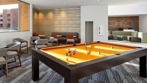 A modern lounge area with a pool table, comfortable seating, and a view of the cityscape through large windows. - Spacious newly built 2-bedroom condo with AC in charming Moab (Moab)