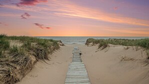 Une promenade en bois menant à la plage, entourée de dunes de sable et de végétation.