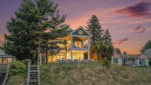 Une maison à deux étages avec un balcon, entourée d’arbres et d’une pelouse.