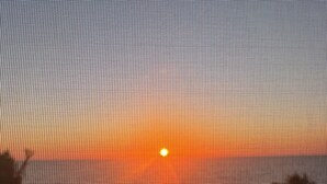 Tramonto su un corso d'acqua, visto attraverso una finestra con motivi a griglia.