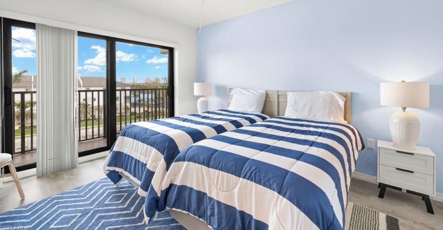 Una camera d'albergo con un letto grande, due lampade sui comodini, un tavolino e vista sull'esterno tramite una porta scorrevole.