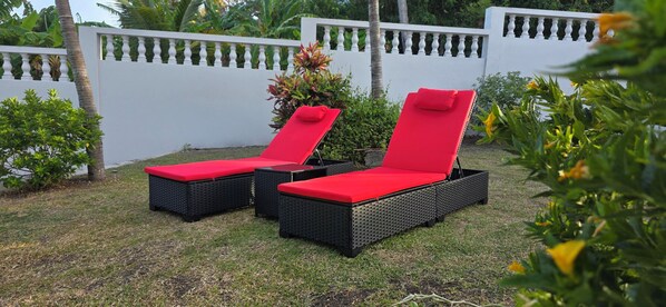 Two outdoor lounge chairs with red cushions, black wicker frames, and a white fence in the background.