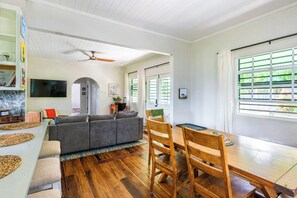 A spacious living area with a gray sofa, wooden dining table, and a ceiling fan.