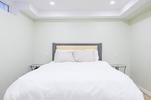 A neatly made bed in a room with a simple headboard and two bedside tables.