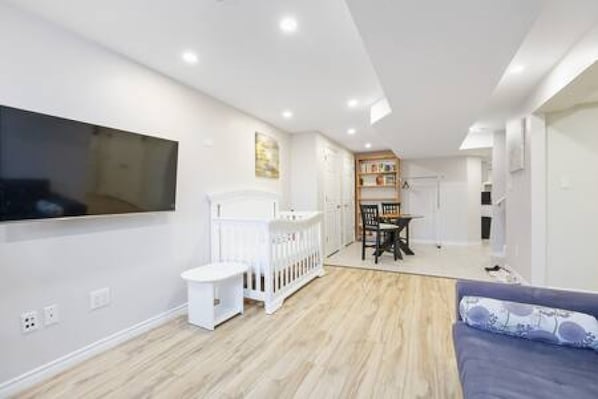 A modern living room with a flat-screen TV mounted on the wall, a white radiator, a dining area with a table and chairs, and a blue sofa.