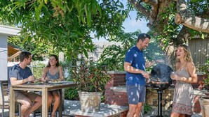 Une terrasse extérieure avec un espace barbecue en briques, une table à manger et des plantes en pot.