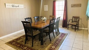 A dining room with a wooden table and chairs, a rug, and a window with curtains.