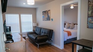 Un espacio habitable compacto con sofá, cama, una mesita y una pequeña cocina.
