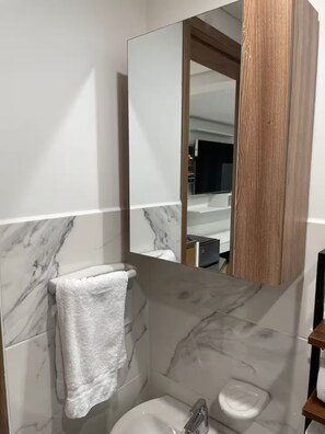 A modern bathroom with a marble wall, a white sink, a toilet, and a wooden vanity. - Entire rental unit in Cali, Colombia Chipichape living … In Heaven (Cali)
