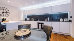 Una cocina moderna con gabinetes blancos, un salpicadero negro y un comedor con mesa y sillas de vidrio.