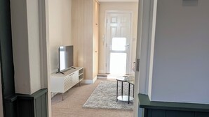 Corredor que dá para um quarto com televisão, radiador e porta com painel de vidro jateado.