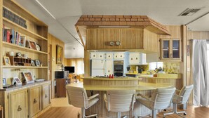 Una cocina con armarios de madera, una isla central con sillas y un microondas.