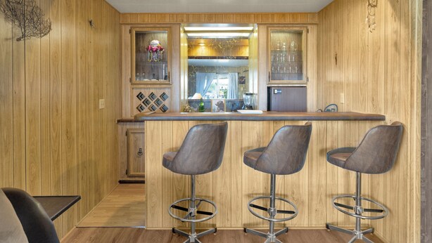 Una cocina con paneles de madera, una zona de bar, tres taburetes y un refrigerador.