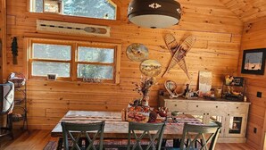 Interior de cabana de madeira, com mesa de jantar posta para quatro pessoas, luminária de cristal e diversas decorações nas paredes.