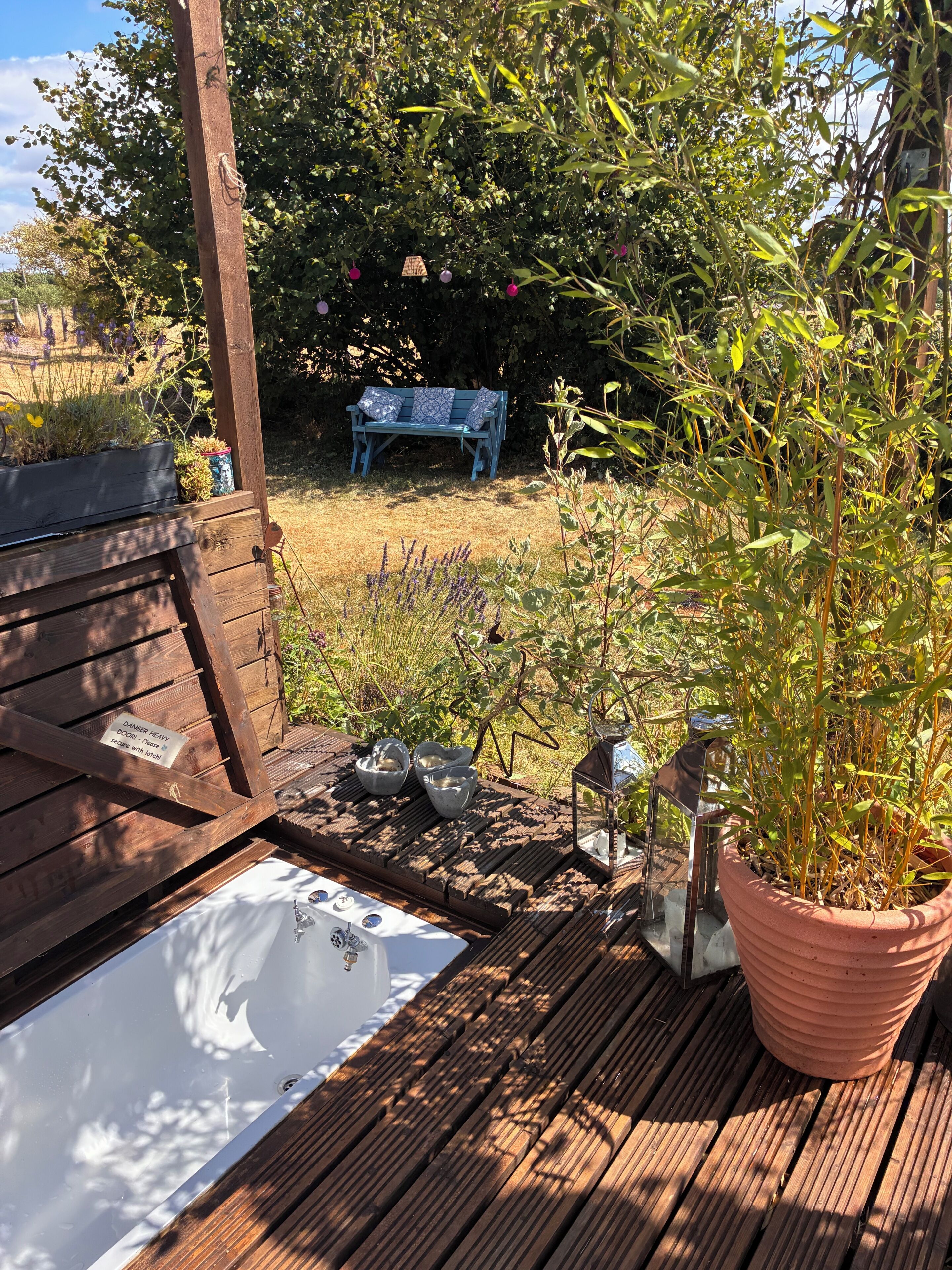 A wooden deck with a bench, a hot tub, and a potted plant.