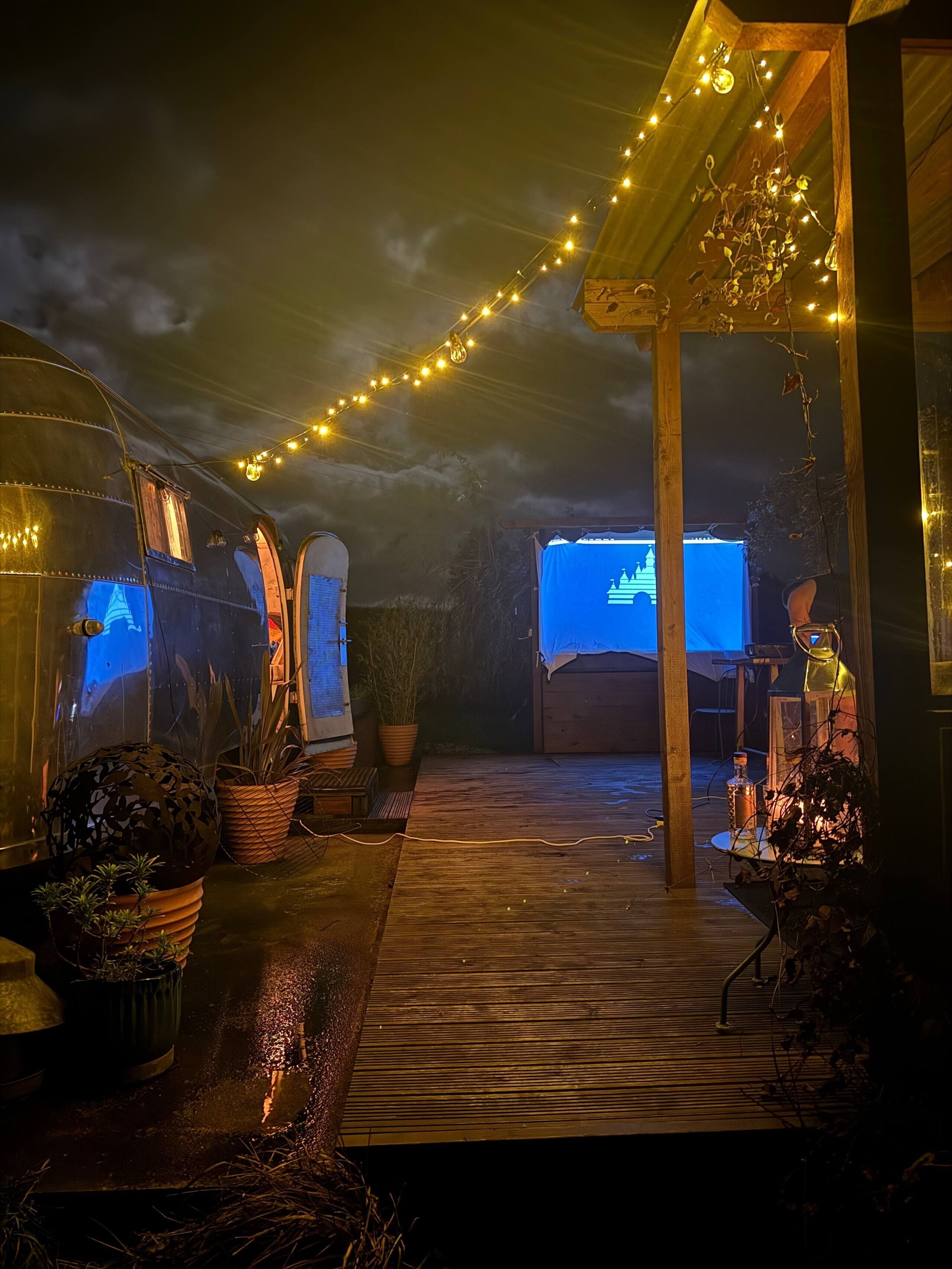 A covered outdoor area with string lights, potted plants, and a projection screen displaying a castle.