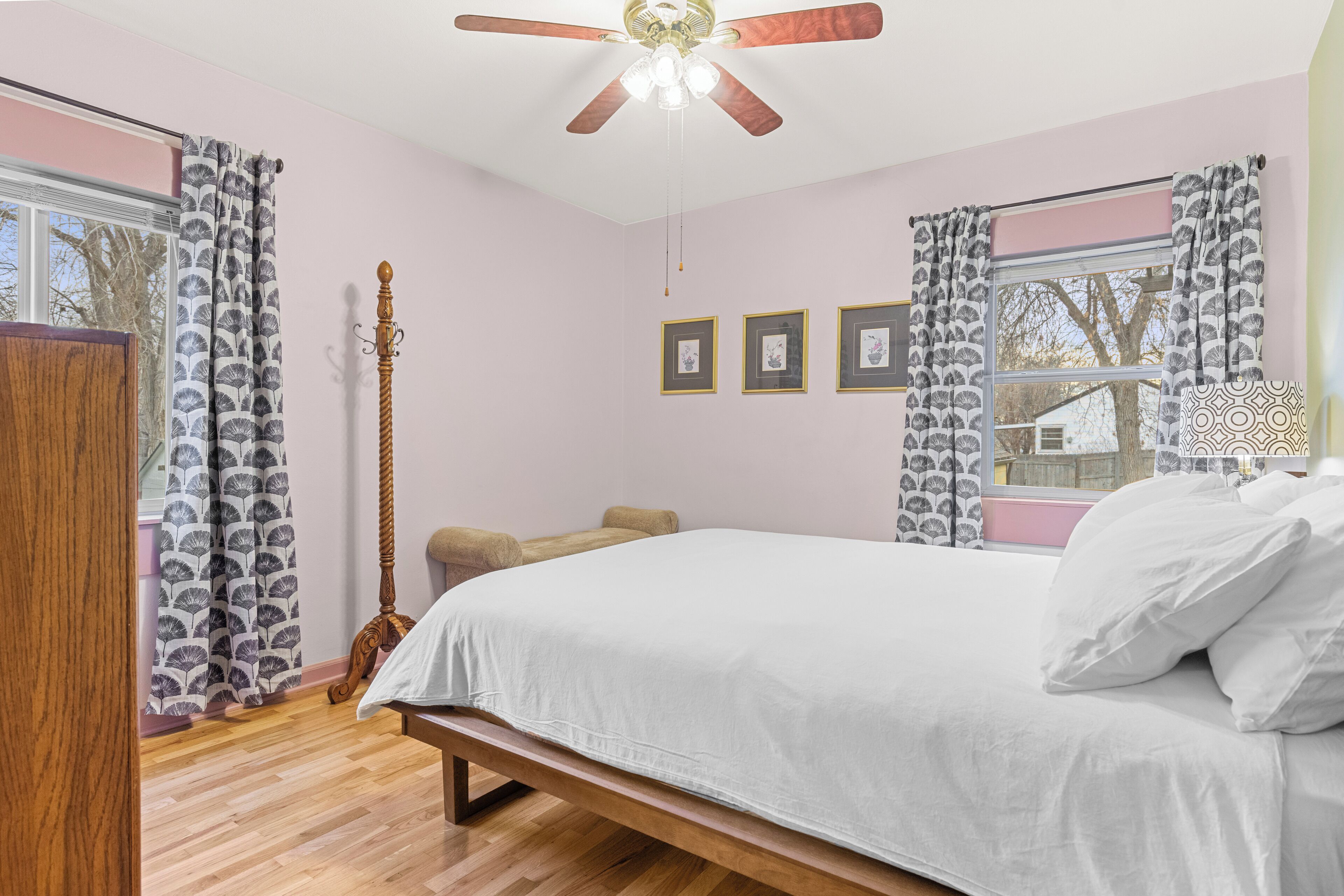 Une chambre à coucher avec un lit, un plancher en bois, un ventilateur de plafond et des rideaux.