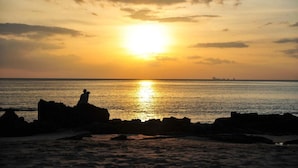 Un tramonto sull'oceano con formazioni rocciose in primo piano.