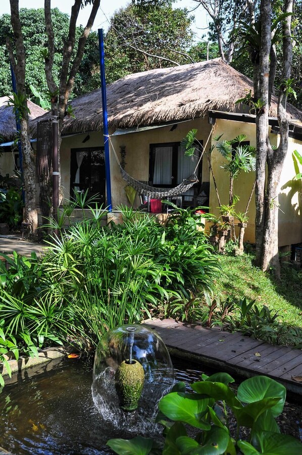 A thatched-roof hut with a hammock, surrounded by lush greenery and a small pond with a decorative vase. - Lalaanta Hideaway Resort (Ko Lanta)