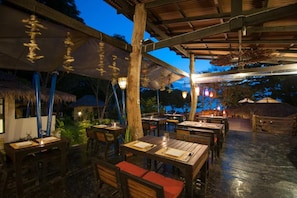An outdoor dining area with wooden tables and chairs, thatched umbrellas, and hanging lanterns. - Lalaanta Hideaway Resort (Ko Lanta)