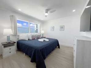 Ein Schlafzimmer mit Bett, Nachttisch, Schreibtisch, Deckenventilator und Fenster mit Blick.