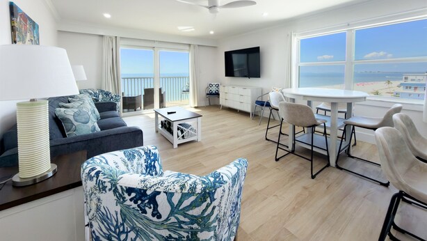 A modern living room with a sofa, chairs, a coffee table, a TV, and a balcony with a view of the sea. - Gateway Villas #899 "Sunset Beach Penthouse" (Fort Myers Beach)