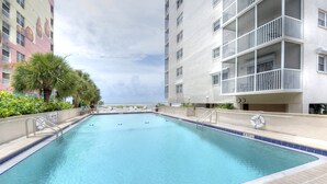 A rectangular swimming pool with a tiled edge, surrounded by a low wall. There are lounge chairs and a palm tree along the poolside. - Gateway Villas #899 "Sunset Beach Penthouse" (Fort Myers Beach)