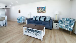 A modern living room with a blue sofa, patterned armchairs, a coffee table, and a painting on the wall. - Gateway Villas #899 "Sunset Beach Penthouse" (Fort Myers Beach)