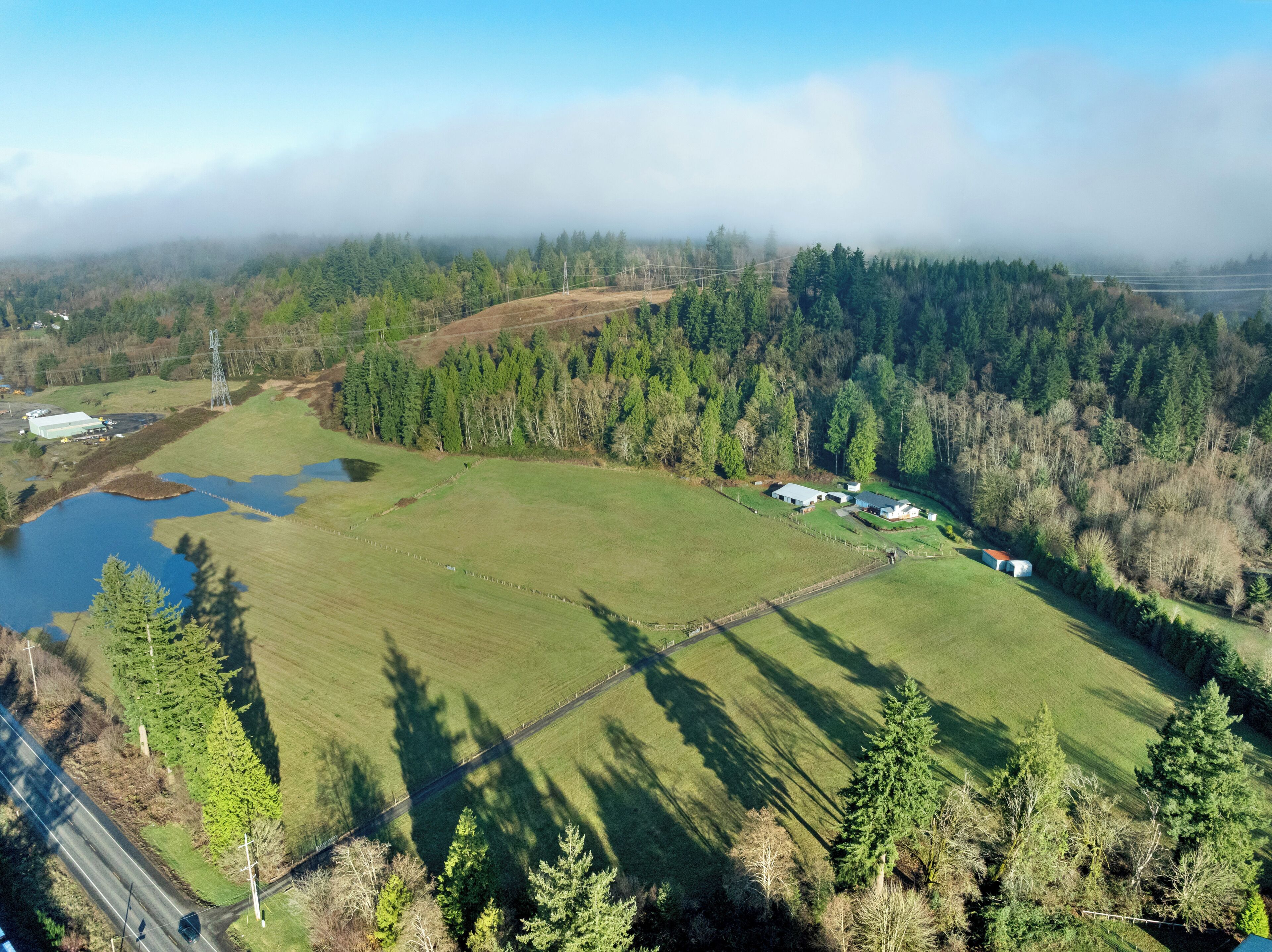 An aerial view of a rural property with a large open field, a small pond, and a few buildings.