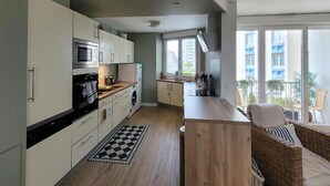 A modern kitchen with white cabinets, a microwave, and a wooden countertop. There is a checkered rug on the floor and a wicker chair near the window. - Superbe appartement vue mer (Dunkerque)