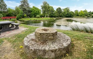 Ein Steins Denkmal in einem Park mit Teich und einer roten Brücke im Hintergrund.