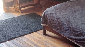 Een slaapkamer met een bed, een bankje, een donkere wand en houten vloeren.