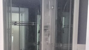 Douchecabine in hoekopstelling met een glazen deur en metalen handgreep.