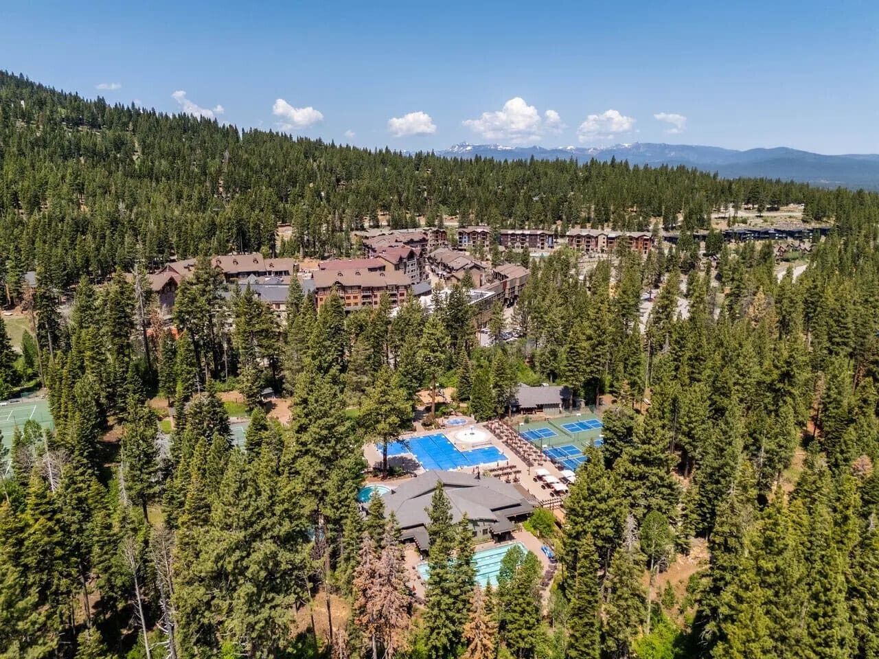 Um resort com vários edifícios rodeados por floresta densa, com piscinas ao ar livre e campos de tênis.