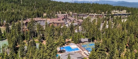 A resort with multiple buildings surrounded by dense forest, featuring outdoor pools and tennis courts.