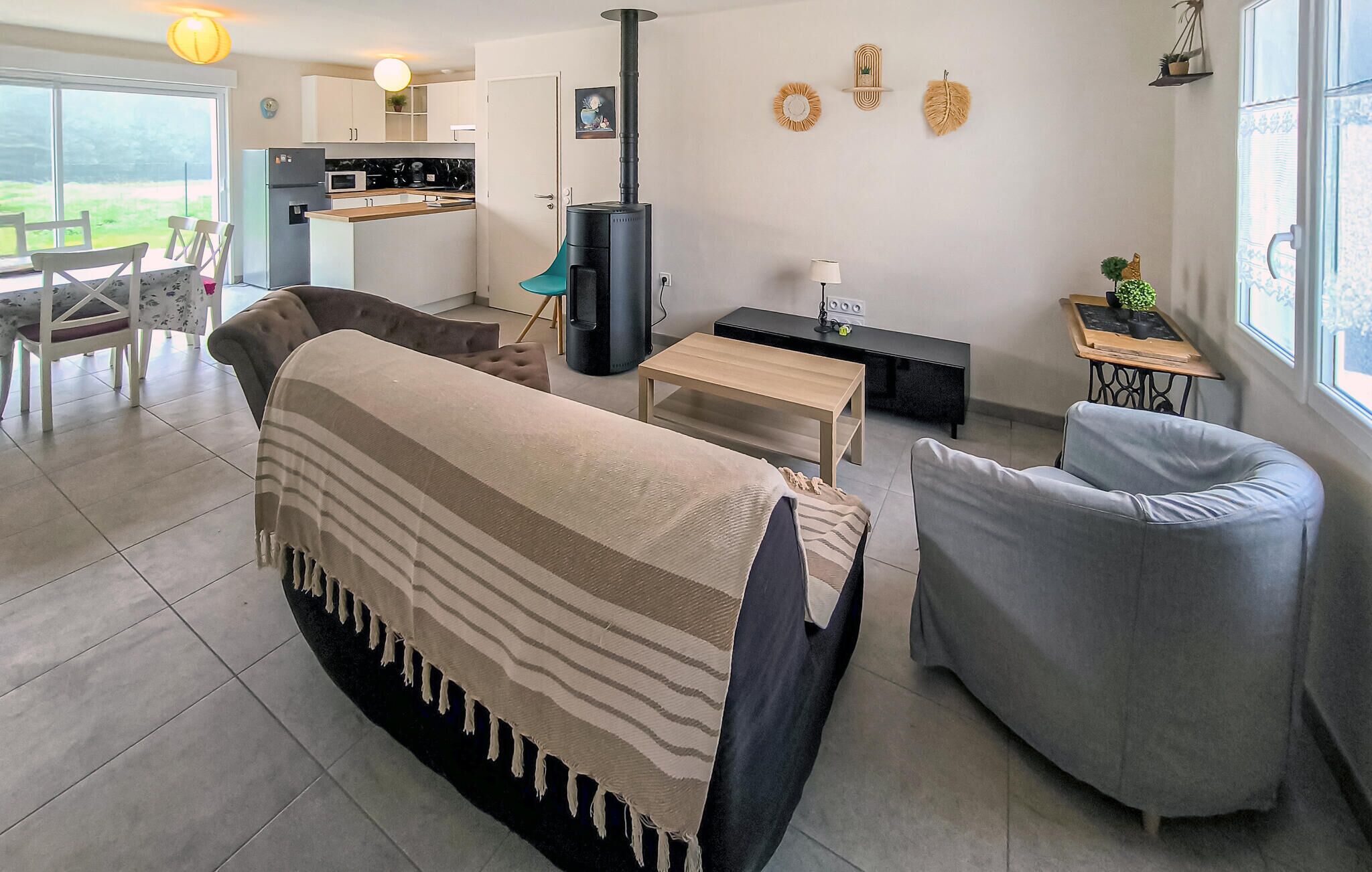 Ein modernes Wohnzimmer mit einer Couch, einem Sessel, einem kleinen Tisch und einer Küche im Hintergrund.