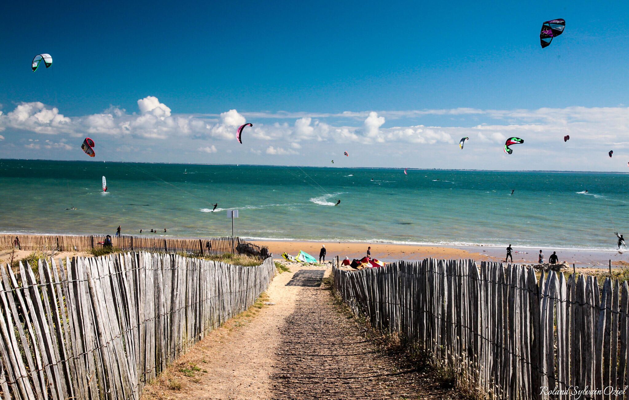 Une plage bordée d’une clôture en bois, offrant une vue dégagée sur l’océan.