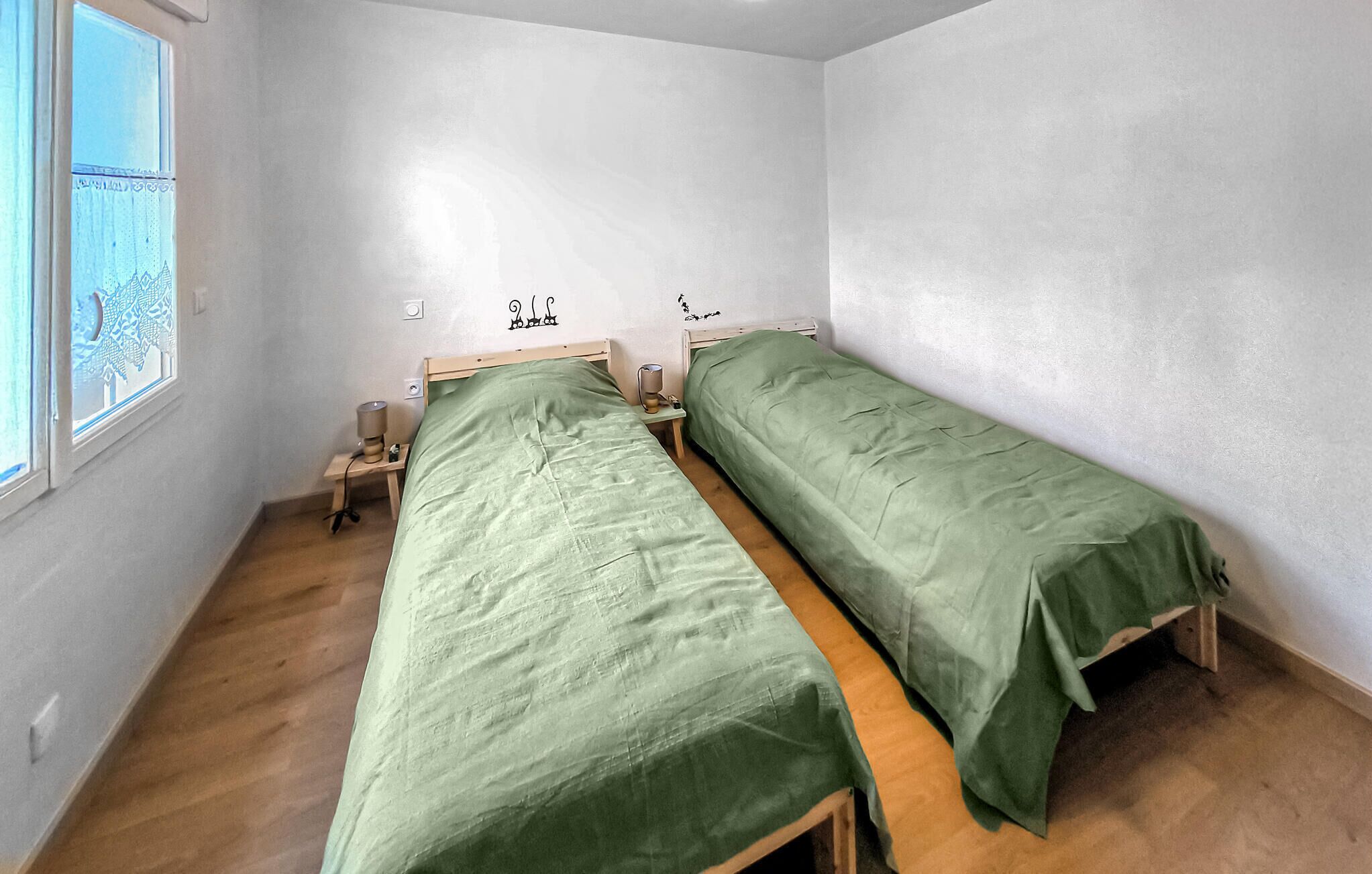 Une petite pièce simple, avec deux lits simples, une table de chevet avec une lampe et une fenêtre donnant sur des arbres.