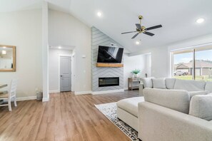 A spacious living room with a fireplace, a ceiling fan, and a large window offering a view of the outdoors. - TV Per Room, 3bd Centrally Located Near Ft Riley (Manhattan)
